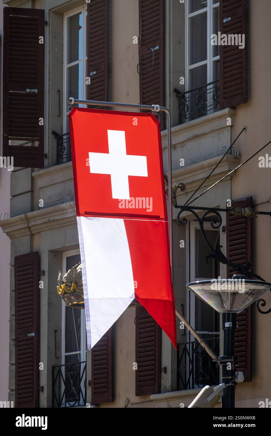 Eine rot-weiße Schweizer Flagge hängt am Gebäude in Morges. Dunkelbraune Fensterläden sind an den Fenstern. Das Gebäude hat einen klassischen europäischen Archit Stockfoto