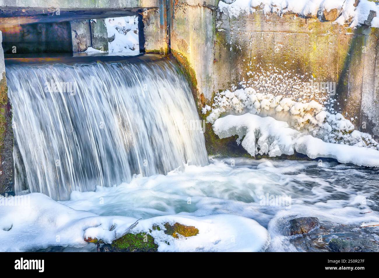 Landschaftsfoto eines nicht gefrorenen Flusses mit schneller Strömung und Stromschnellen an düsteren kalten Wintertagen. Kleiner Wasserfall mit Bewegungsunschärfe Stockfoto