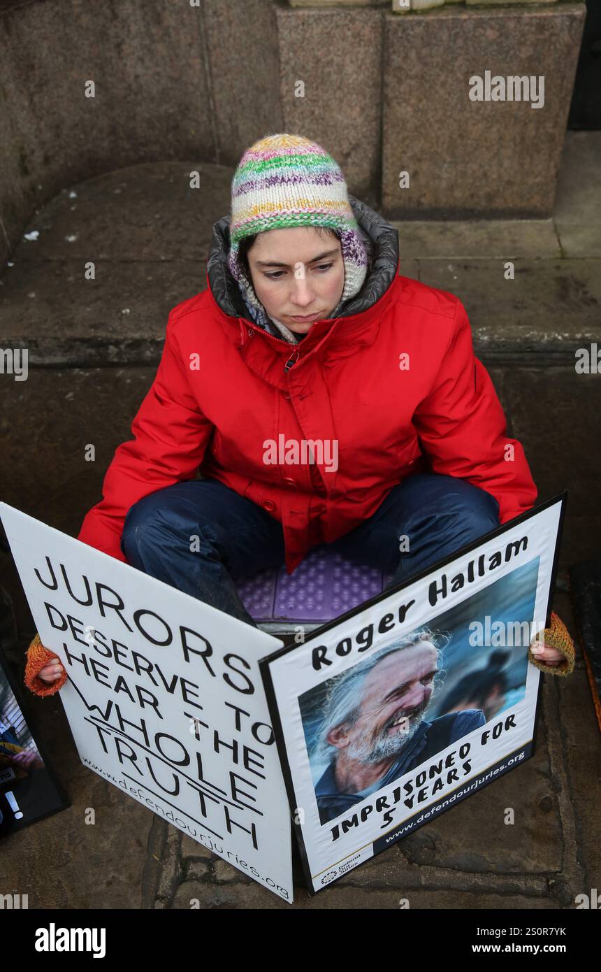 Ein Befürworter der Verteidigung unserer Jurys hält Plakate mit der Aufschrift "Geschworene verdienen es, die ganze Wahrheit zu hören" und ein Fotozeichen von Roger Hallam, der derzeit eine Strafe von fünf Jahren verbüßt, während der Mahnwache. Demonstranten, die unsere Geschworenen verteidigen, sitzen vor der Guildhall auf dem Marktplatz von Cambridge, um auf die Not von 41 politischen Gefangenen hinzuweisen, die wegen friedlicher Maßnahmen zur Unterstützung Palästinas und des Klimanotfalls inhaftiert sind. Stockfoto