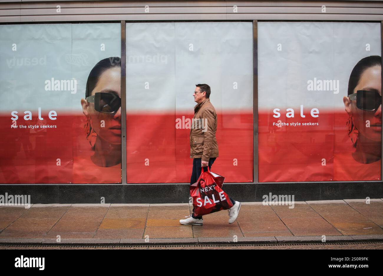 Cambridge, Großbritannien. Dezember 2024. Ein Käufer geht an den „Sale“-Schildern im Marks&Spencers-Fenster vorbei und trägt eine Tasche mit dem nächsten Verkauf. Trotz der schlechten Wirtschaftsleistung in den letzten Monaten des Jahres 2024 und der drohenden Rezession gehen Käufer auf die Straße, um die Vorteile der Weihnachtsverkäufe im Stadtzentrum von Cambridge zu nutzen. Quelle: SOPA Images Limited/Alamy Live News Stockfoto