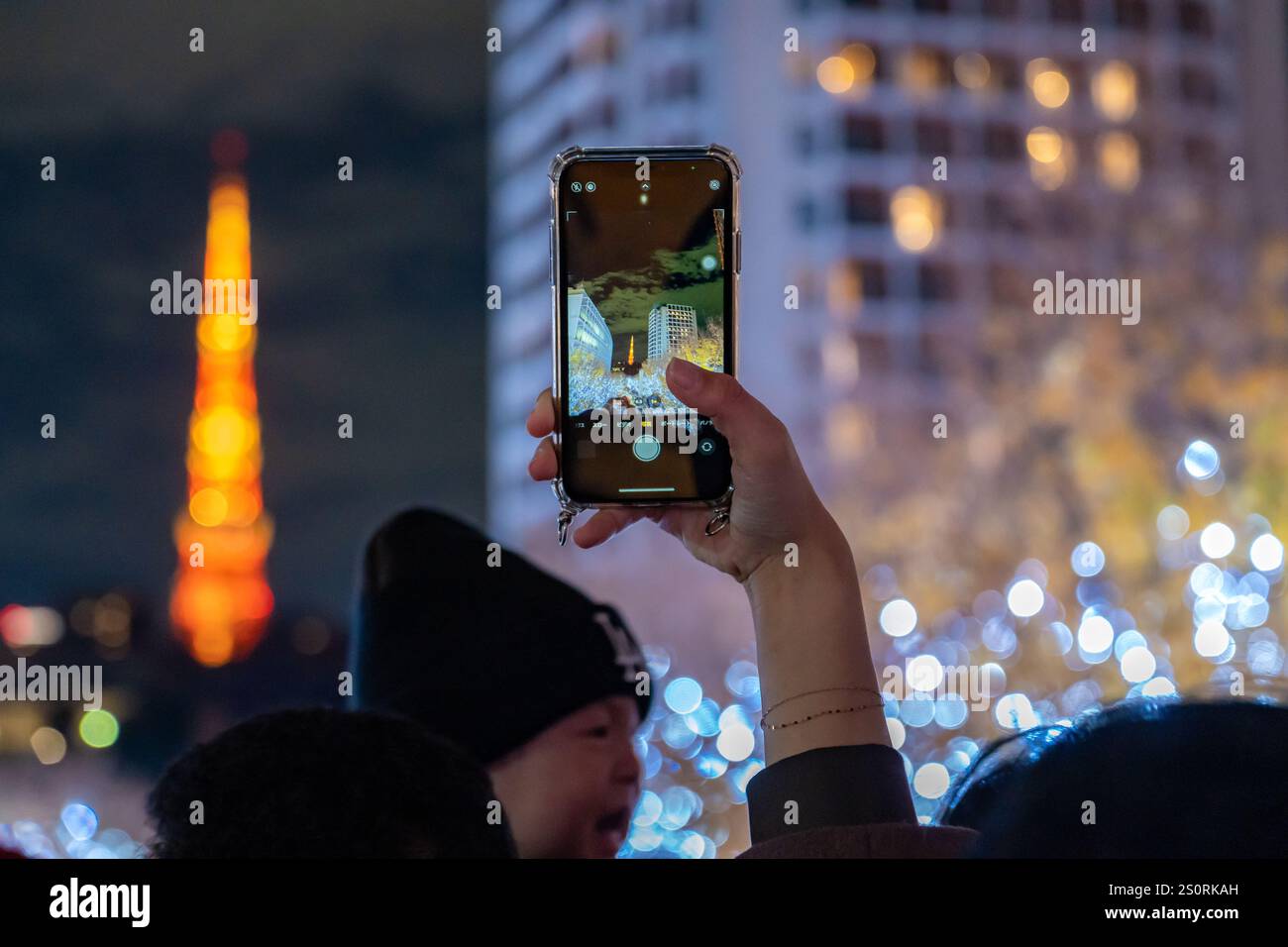 Tokio, Japan - 14. Dezember 2024 - Nahaufnahme einer Hand, die eine Schrift hält, um die dekorierten Lichter und den wunderschönen Tokyo Tower bei Nacht zu fotografieren Stockfoto