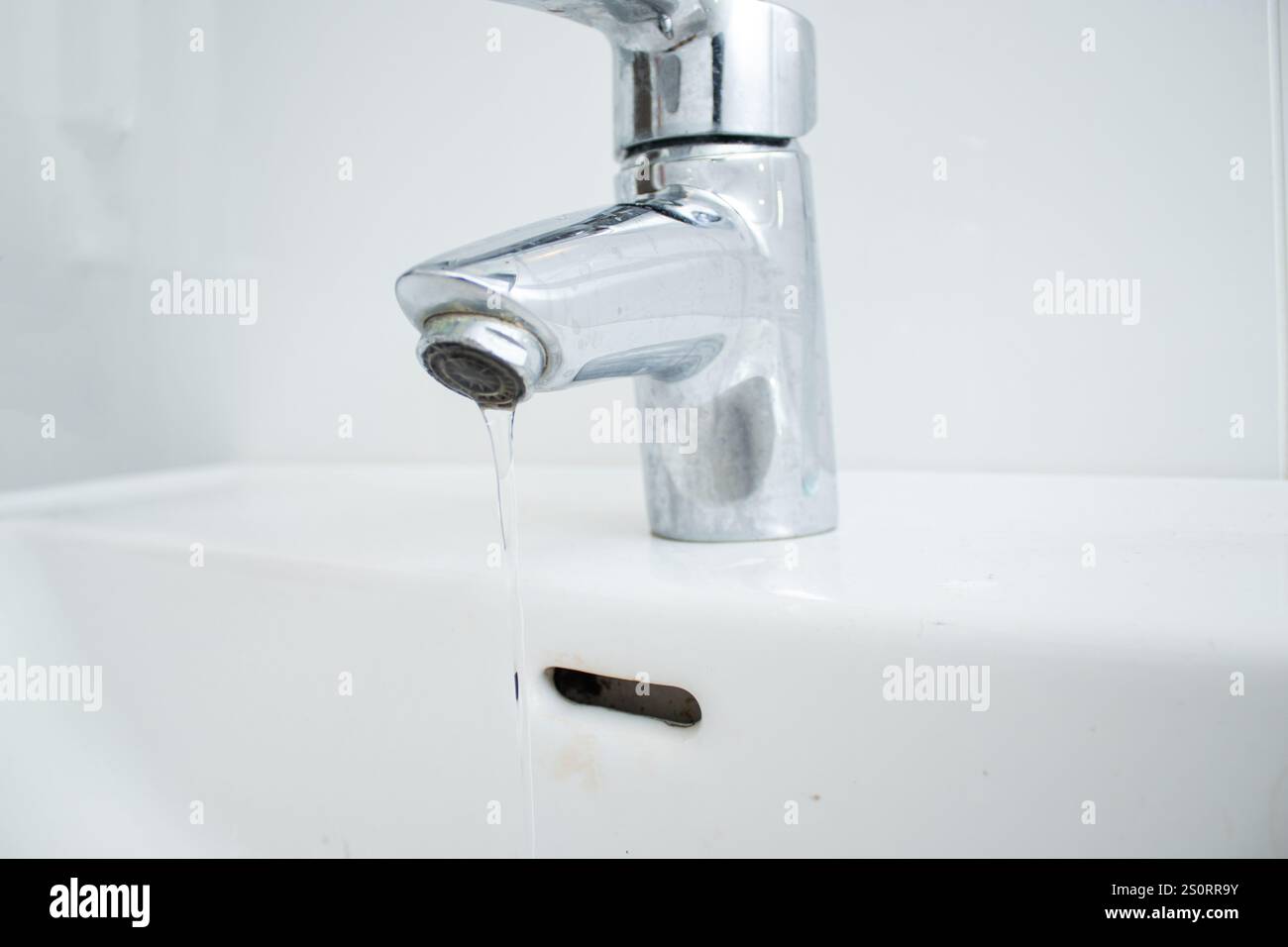 Nahaufnahme einer Armatur im Badezimmer mit fließendem Wasser und Kalkflecken und schmutzigem Waschbecken Stockfoto