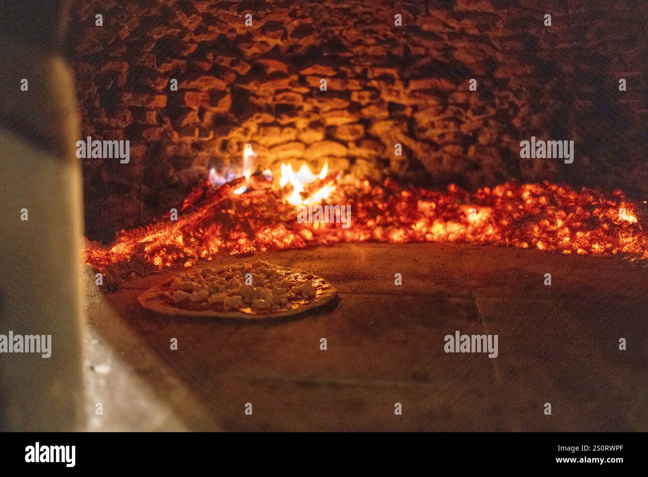 Eine Pizza voller Beläge, die in einem traditionellen Holzofen gebacken wird, umgeben von glühender Glut und Flammen. Stockfoto Eine Pizza voller Beläge, die in einem traditionellen Holzofen gebacken wird, umgeben von glühender Glut und Flammen. Stockfoto
