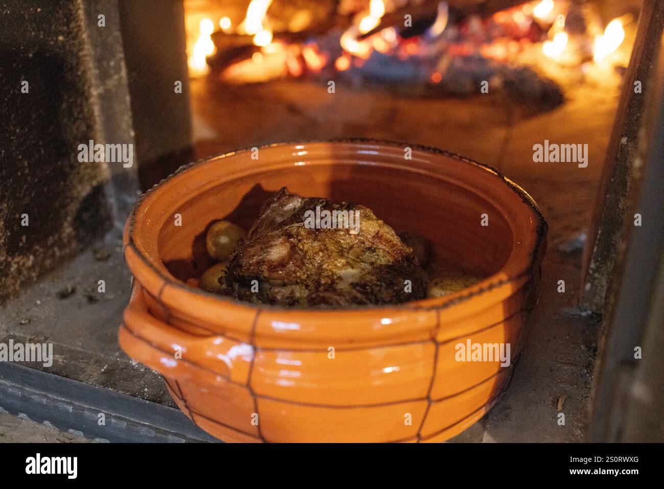 Ein rustikaler Tontopf gefüllt mit gebratenem Fleisch und Kartoffeln, in einem traditionellen Holzofen. Stockfoto