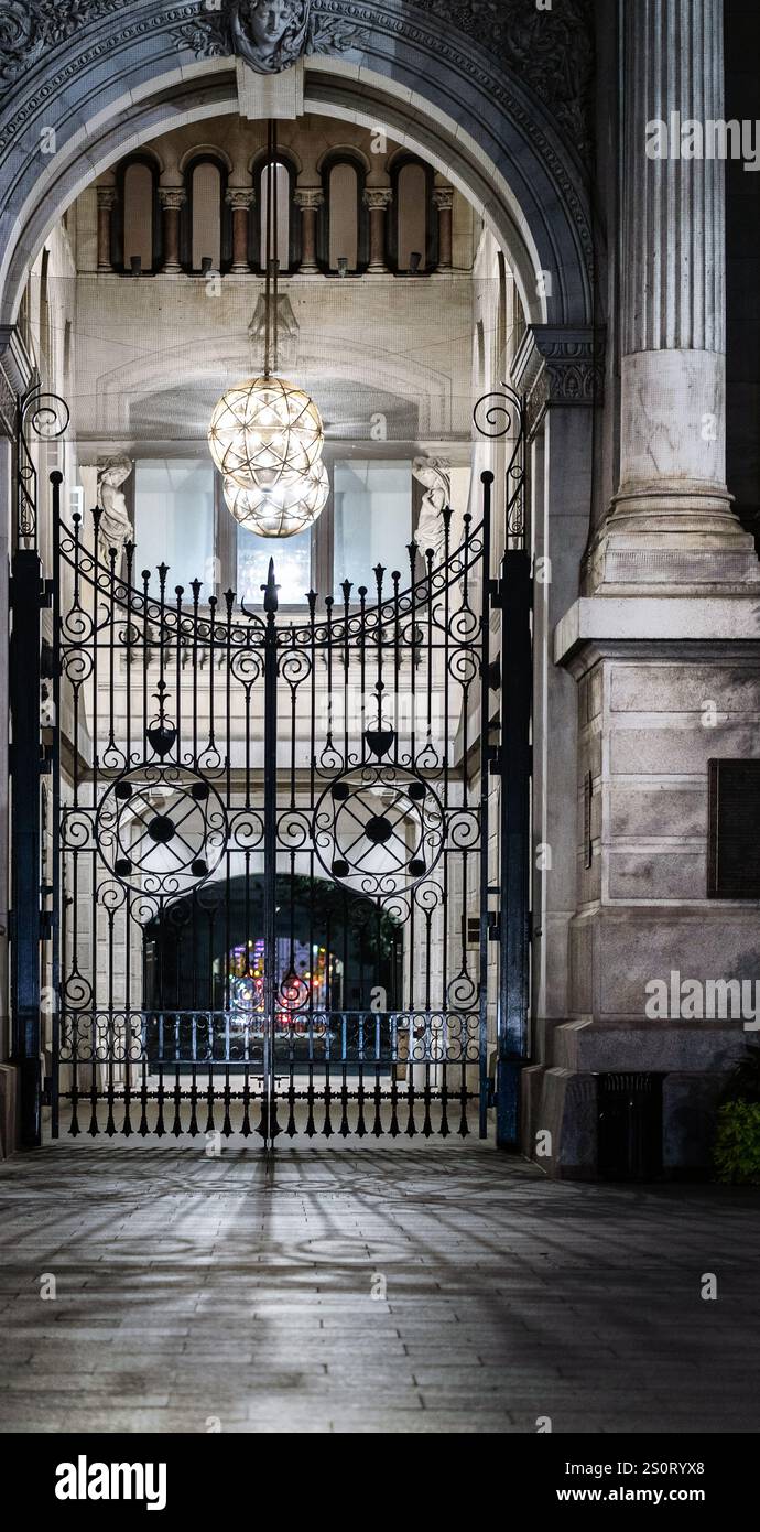 Ein großer Eingang mit kunstvollen schmiedeeisernen Toren, flankiert von klassischer Architektur. Die Szene wird von einem großen dekorativen Kronleuchter cr beleuchtet Stockfoto