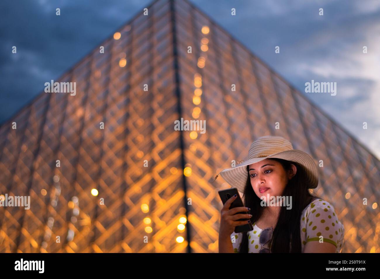 Eine schöne Frau, die vor dem Louvre, einem der größten Museen der Welt und einem historischen Monument, ihr Handy überprüft. Ein zentrales Wahrzeichen von Par Stockfoto