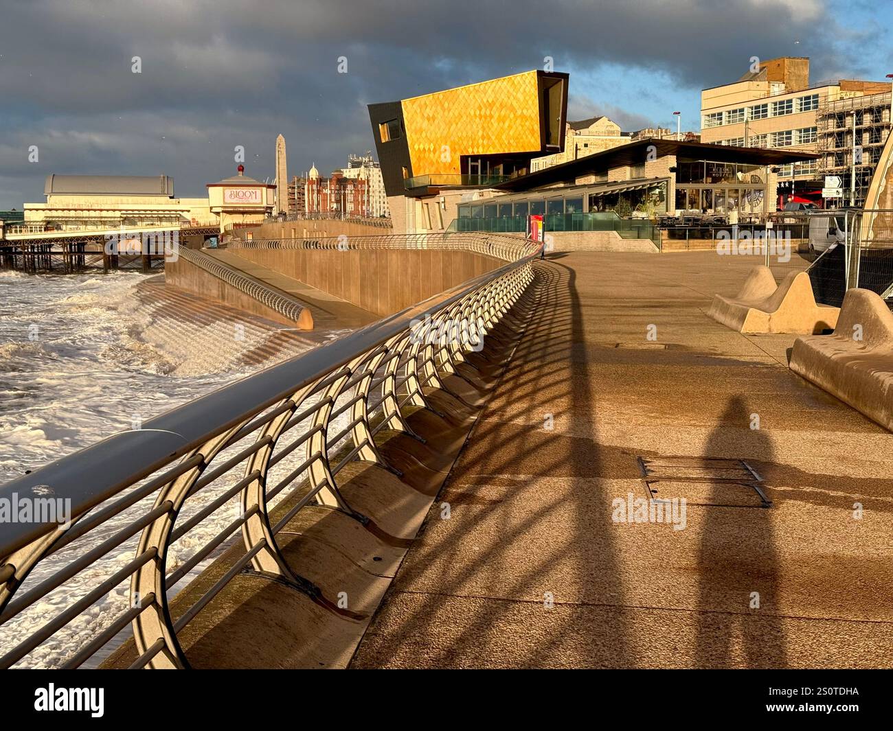 Schatten des Fotografen auf der Blackpool Promenade bei Flut mit goldener Hochzeitskapelle und North Pier in der Ferne Stockfoto