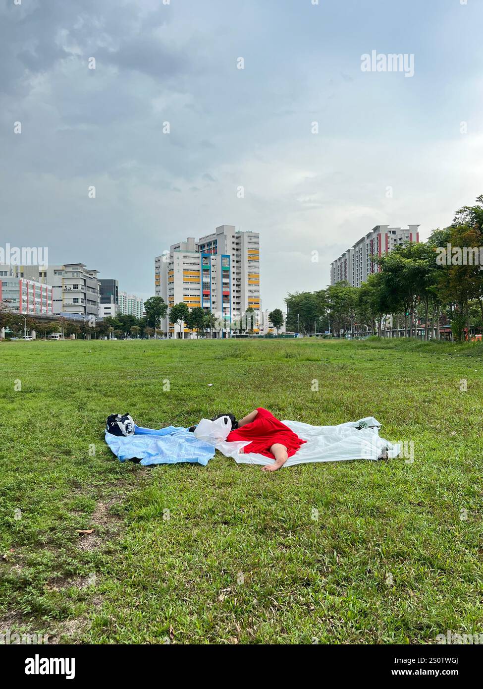 Eine Hausangestellte in rotem Kleid liegt auf einem offenen Feld und schläft während ihres freien Tages am Wochenende. Erholen Sie sich im Grünen. Singapur - Smartphone-aufgenommenes Stockfoto