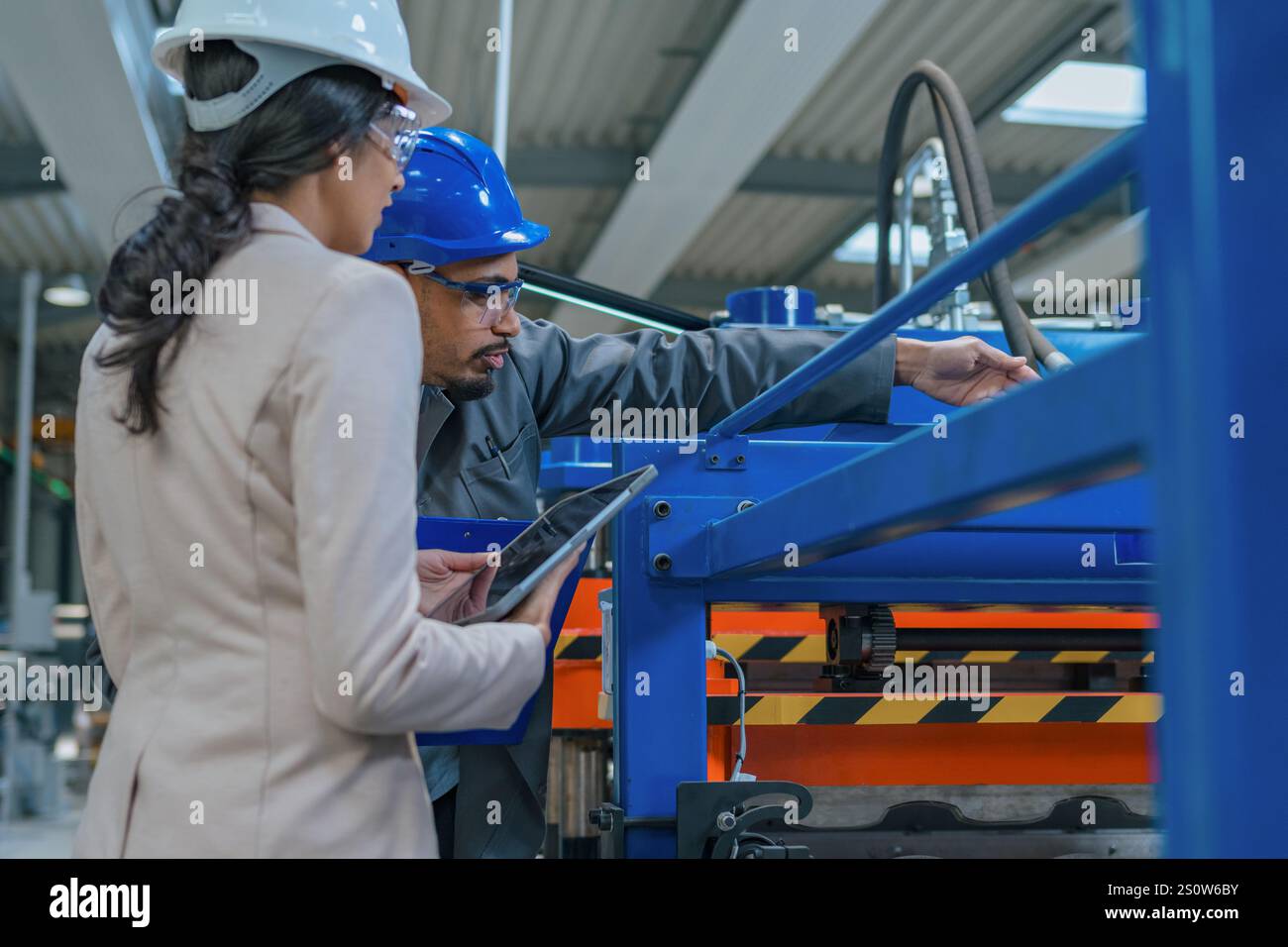 Afroamerikaner Ingenieur und eine Inderin, eine Fabrikleiterin, die ein Tablet hält, durch die Produktionslinie läuft, Inspektionen durchführt, Vorderansicht. Stockfoto