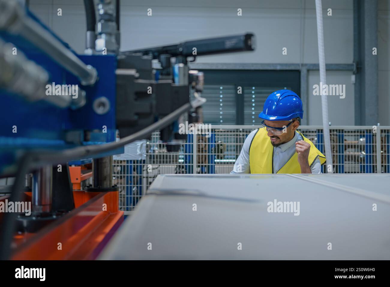 Fertigungsingenieur in einer Fabrik mit gelber Weste und blauem Helm bei der Arbeit. Stockfoto