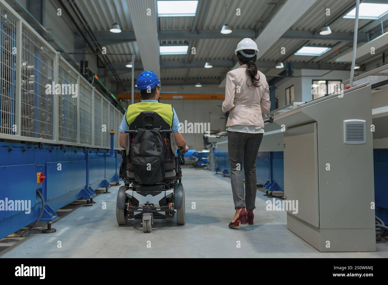 Weibliche Führungskraft, die einen neuen Mitarbeiter mit einer Behinderung für einen Job ausbildet, erklärt die Arbeit an Maschinen. Industrie, Integration und Arbeitsplatzkonzept. Stockfoto