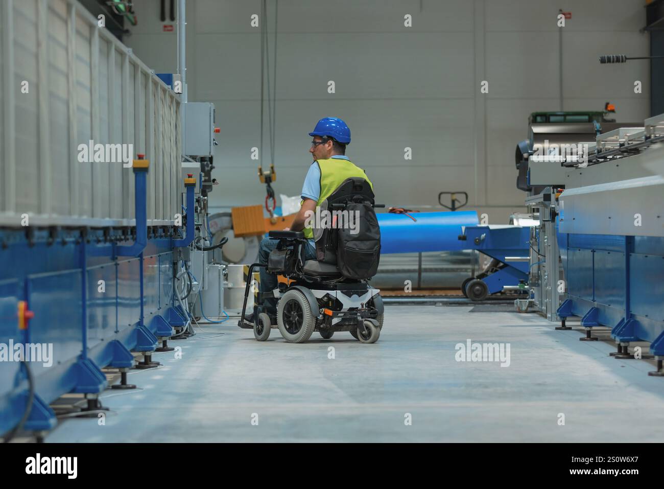 Fertigungsingenieur mit Behinderung in einer Fabrik mit gelber Weste und blauem Helm bei der Arbeit. Stockfoto