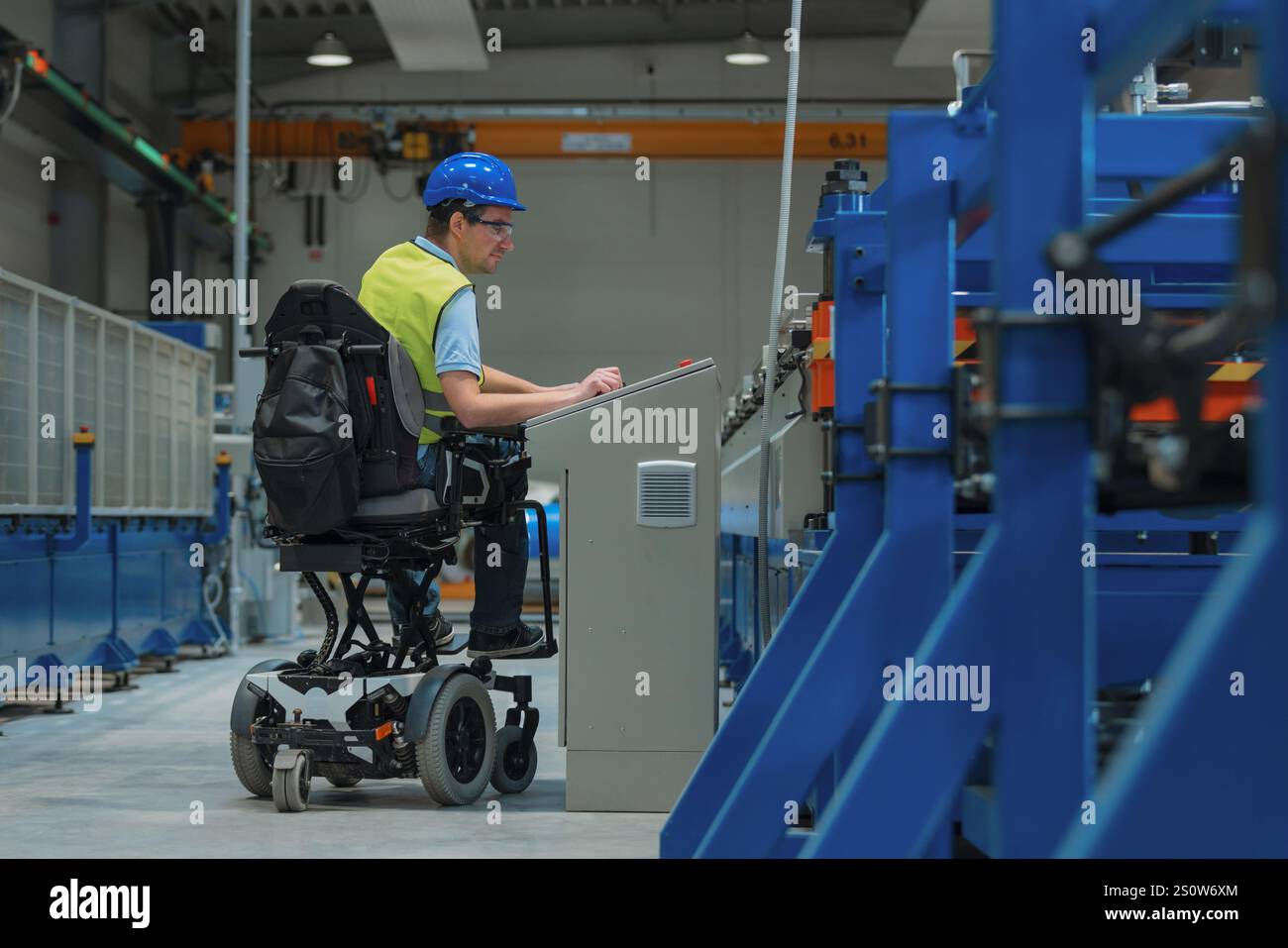 Fertigungsingenieur mit Behinderung in einer Fabrik mit gelber Weste und blauem Helm bei der Arbeit. Stockfoto