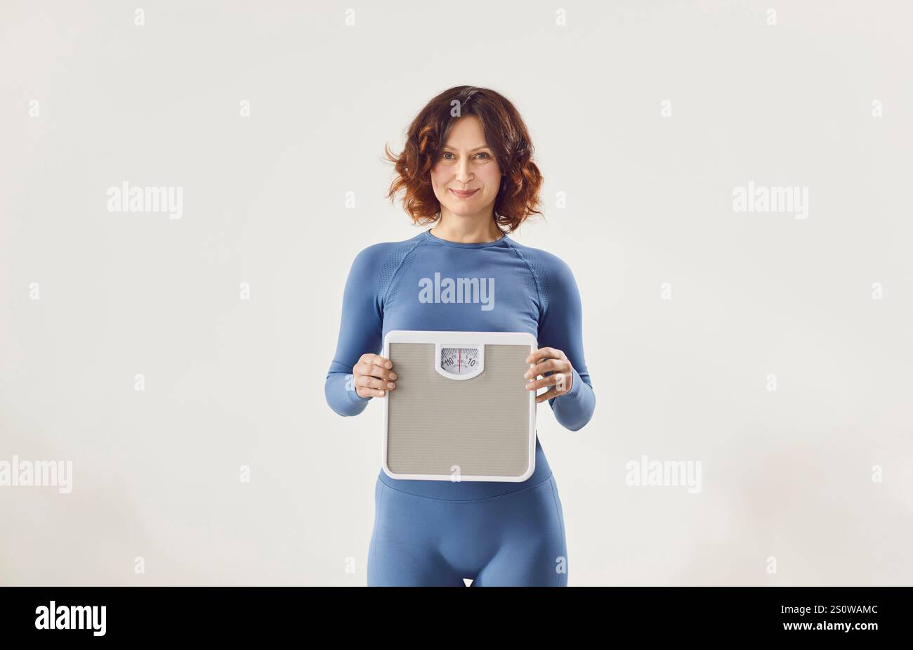 Sportliche Frau, die Waagen hält, nachdem sie ihr Gewicht isoliert in weißem Studio-Hintergrund gemessen hat Stockfoto