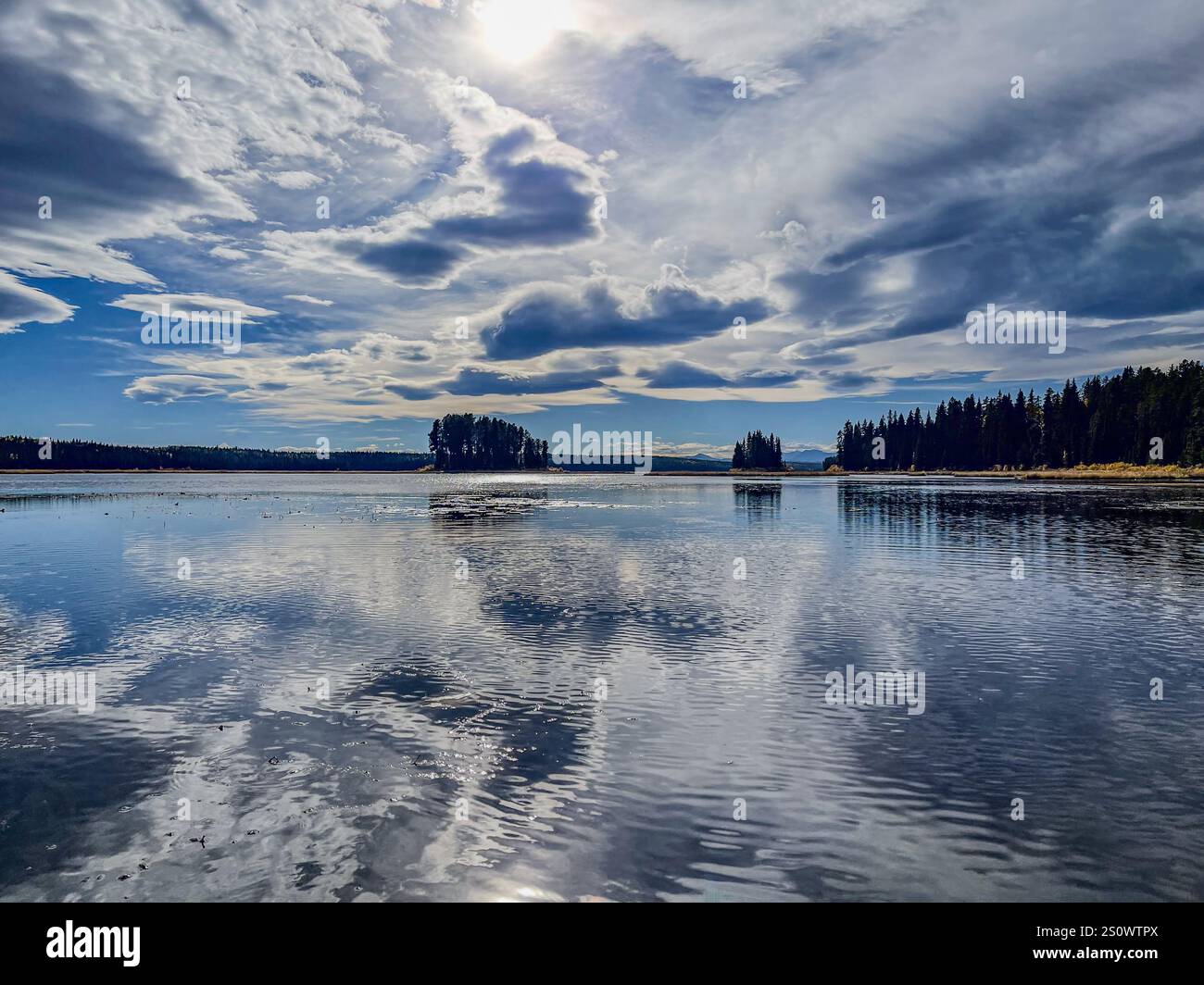 Ein ruhiger See, umgeben von Wäldern, mit Wolken, die sich dramatisch auf der Wasseroberfläche spiegeln. Die beschauliche Landschaft weckt ein Gefühl von Frieden und Natur Stockfoto