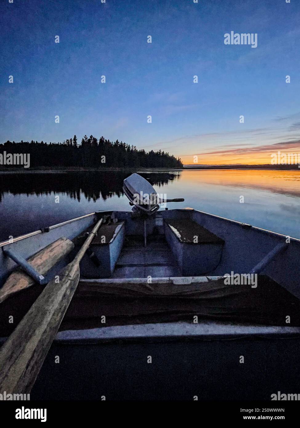 Ein leeres Fischerboot vor Anker auf einem ruhigen See in der Dämmerung, umgeben von Wildnis. Stockfoto
