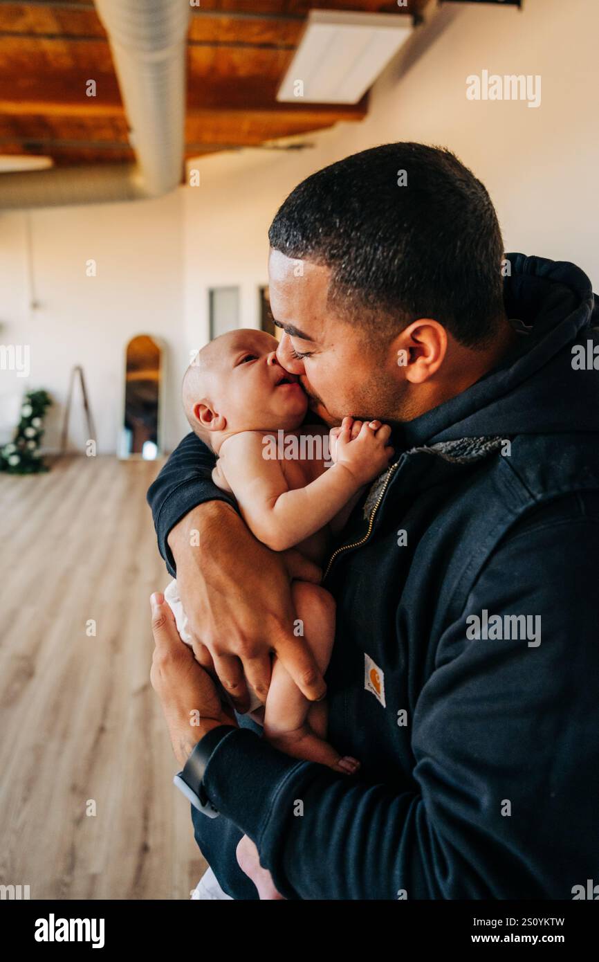 Vater hält und küsst ein Baby in einem gemütlichen, modernen Zuhause Stockfoto