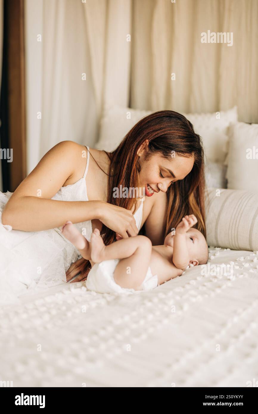 Mutter spielt fröhlich mit ihrem Baby auf einem gemütlichen, weißen Bett Stockfoto
