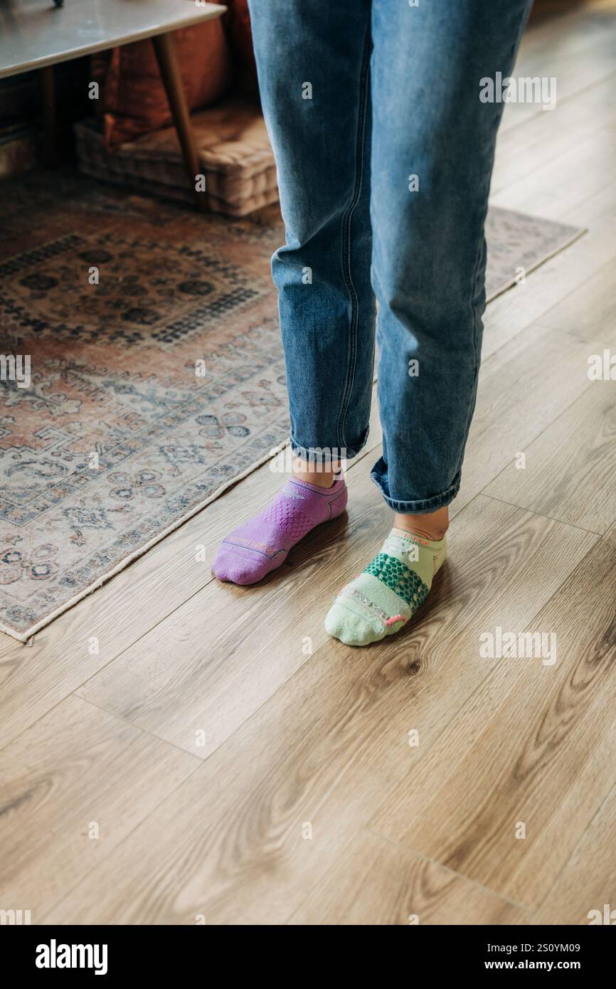 Füße tragen unpassende, bunte Socken auf Holzboden Stockfoto