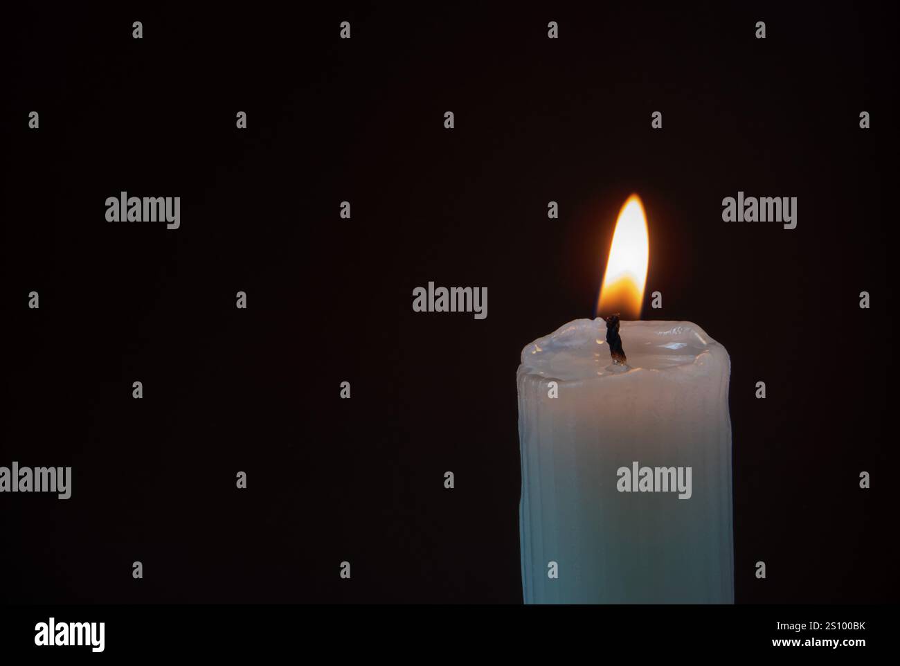 Brennende Kerze aus geripptem Stumpenwachs auf dem dunklen Hintergrund mit Kopierraum. Helle Flamme in der Dunkelheit. Kerzenlicht. Stockfoto
