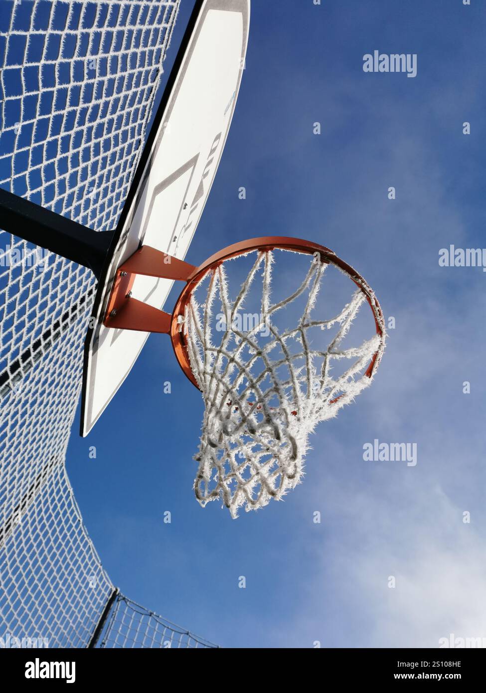 Basketballkorb unter klarem blauem Himmel unterstreicht einen sonnigen Tag, der perfekt für Outdoor-Sportarten ist - Smartphone-aufgenommenes Stockfoto
