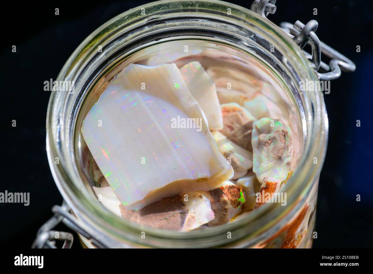 Ein Glasgefäß gefüllt mit verschiedenen Opal- und Mineralfragmenten, die ihre einzigartigen Farben und Texturen zeigen. Das Gefäß ist mit einem Metallklas versiegelt Stockfoto