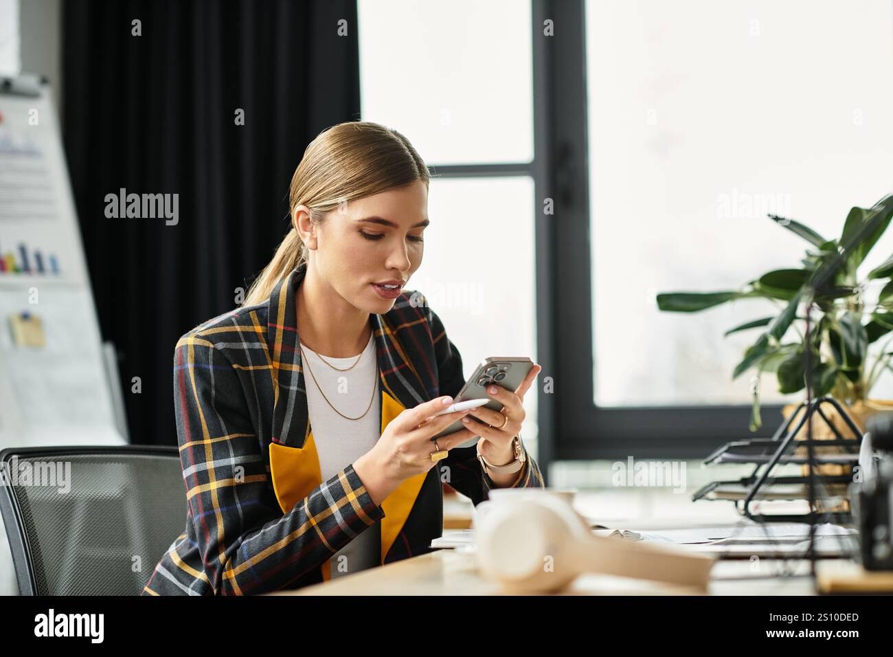 Eine Millennials Geschäftsfrau konzentriert sich auf ihr Smartphone, während sie an einem eleganten Schreibtisch sitzt. Stockfoto