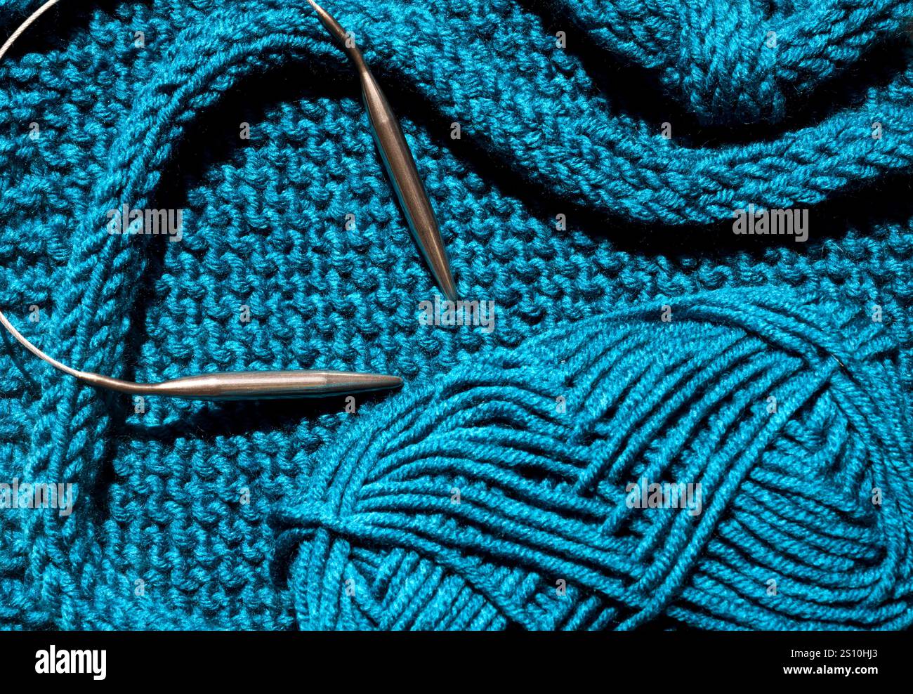 Türkisfarbene Winterstrickbekleidung wird aus Wollgemisch gestrickt. Handgefertigtes Konzept, Hobby, modischer Online-Strickkurs. Stockfoto