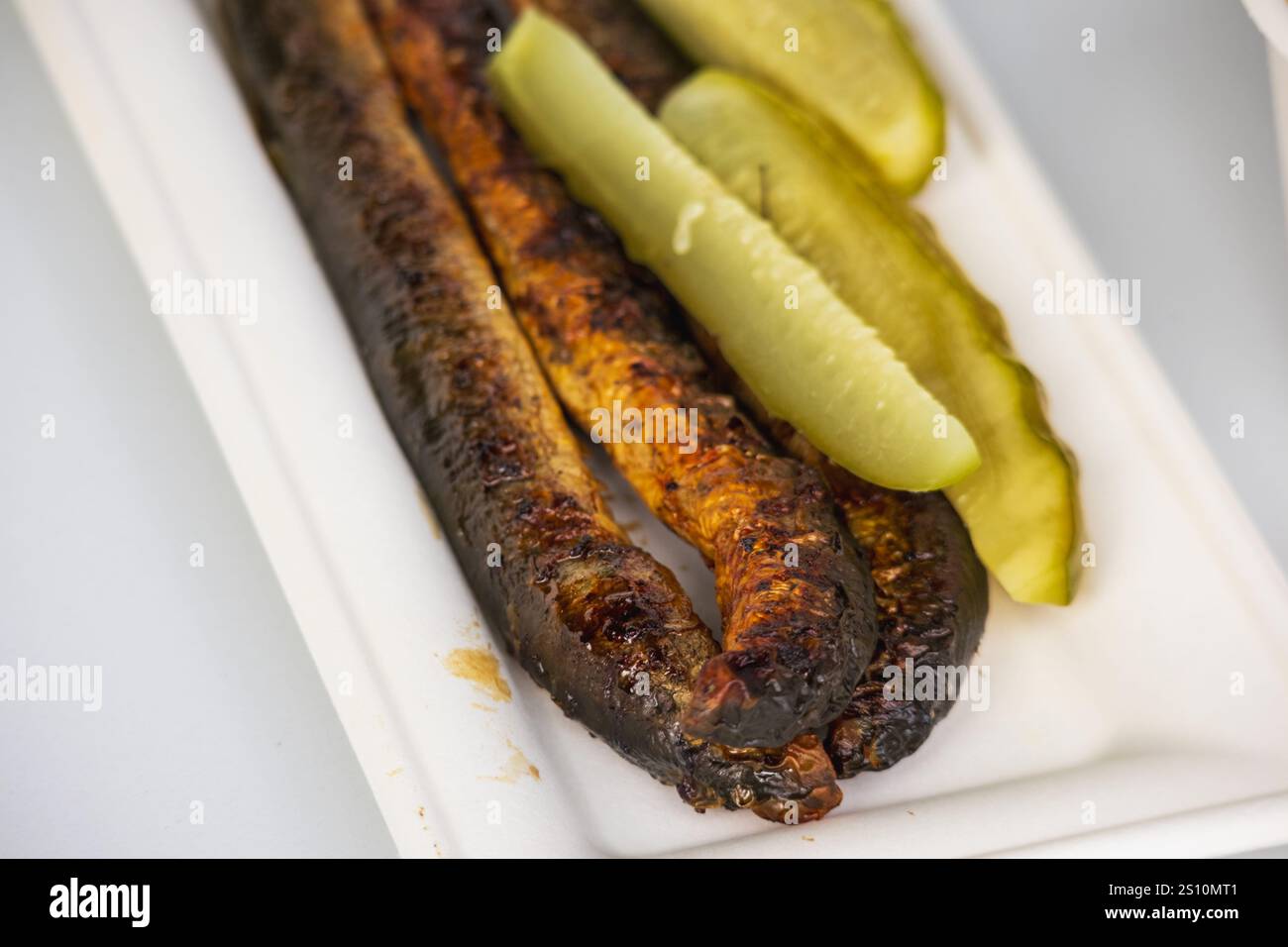 Das Bild zeigt einen Teller mit gebratenem Fisch und Gurken. Der Fisch wird zu einer goldbraunen Kruste gebraten. Eingelegte Gurken werden in Scheiben geschnitten. Stockfoto