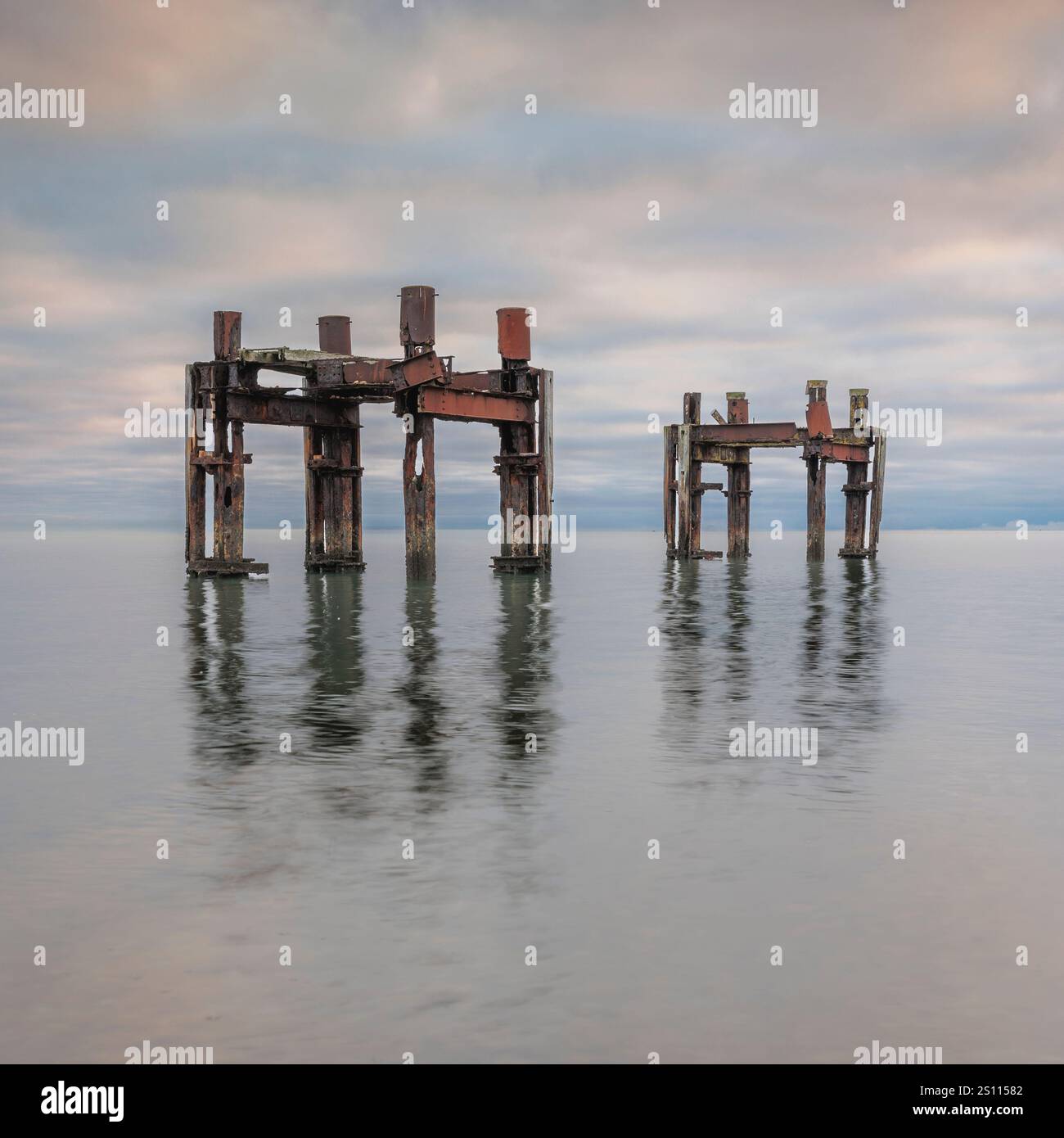 Rostige Überreste des Ladepiers aus der Zeit des Zweiten Weltkriegs in Lepe Beach, Hampshire. Diese „Delfine“ unterstützten Landungen am D-Day. Eine reflektierende Meereslandschaft mit Geschichte, Stockfoto