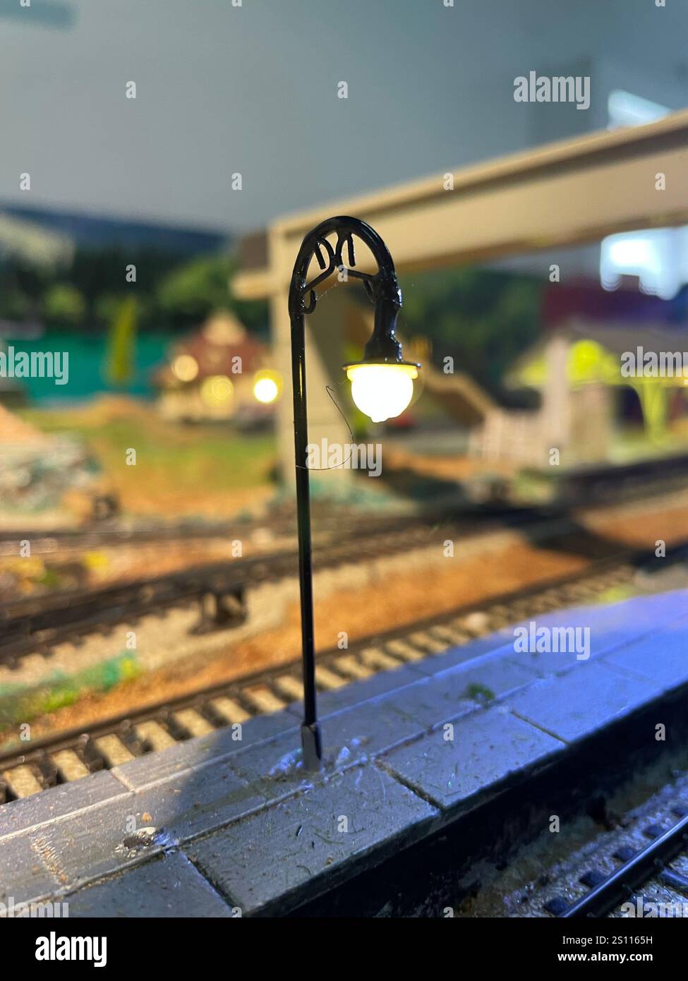 Ein wunderschön detaillierter Bahnhofsbahnsteig mit einer Straßenlaterne im Vintage-Stil, die mit warmem Licht beleuchtet wird. Modelleisenbahn-Layout. - Smartphone-aufgenommenes Stockfoto