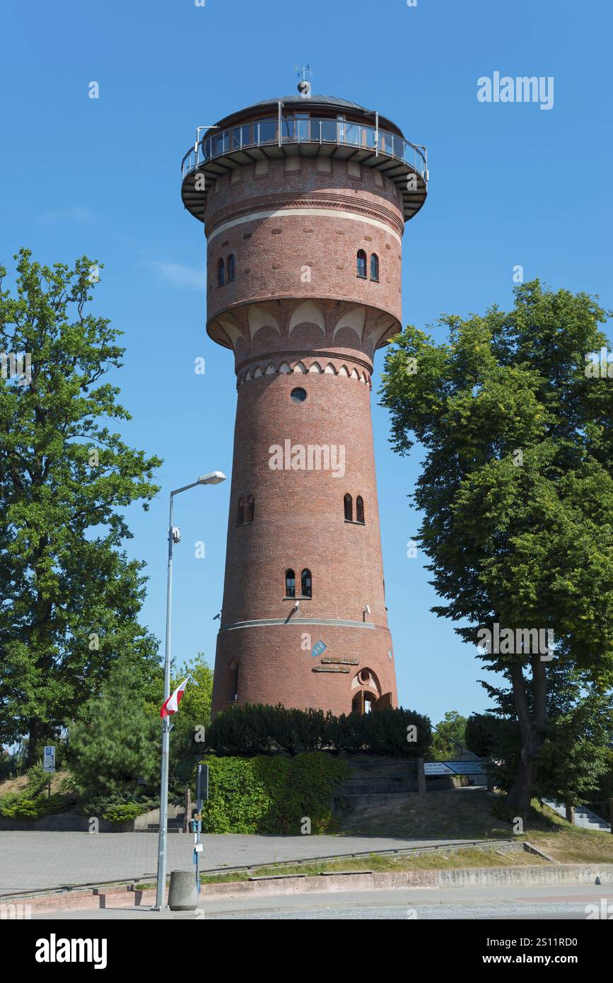 Ein hoher Backsteinwasserturm neben grünen Bäumen unter blauem Himmel, Museum und Café, Wasserturm, Gizycko, Warminsko-Mazurskie, Warminsko-Mazurskie, Polen Stockfoto
