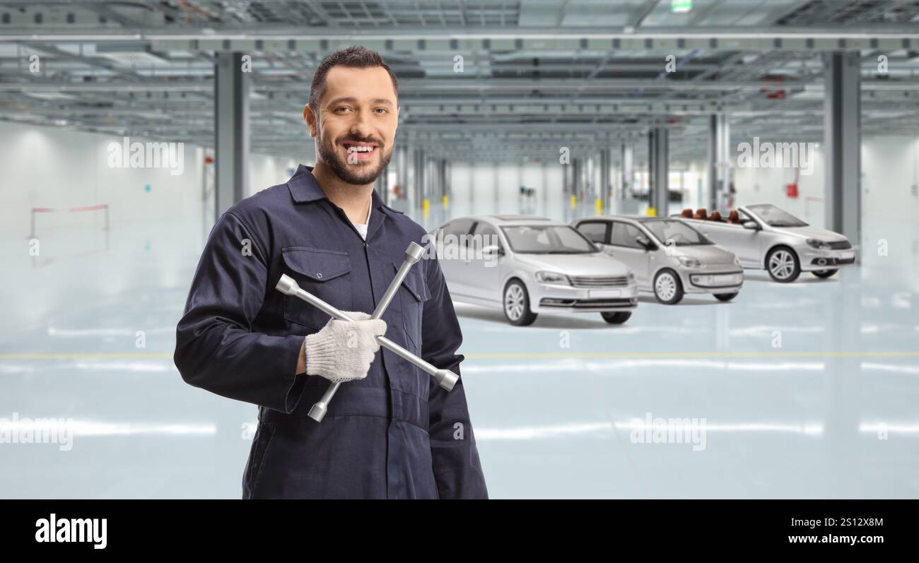 Autowerkstatt mit Fahrzeugen und Automechaniker, der einen Radmutternschlüssel hält Stockfoto