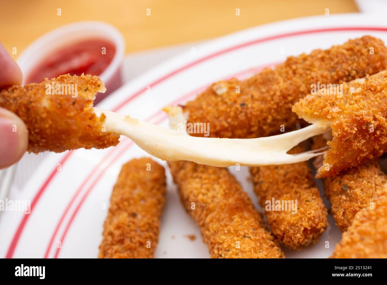Eine Nahaufnahme eines Vorspeisetellers mit frittierten Mozzarella-Sticks, mit einer Hand, die den Käse wegzieht. Stockfoto