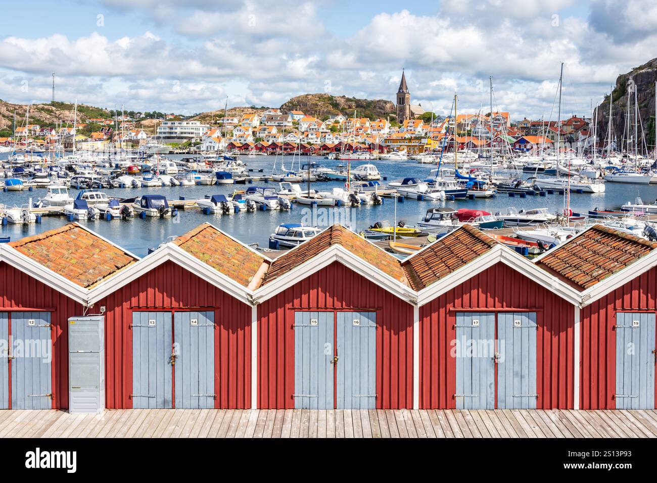 Der Jachthafen und das Dorf Fjällbacka, Schweden, mit Blick auf den Kirchturm, mit Strandhütten im Vordergrund an einem sonnigen Tag. Stockfoto