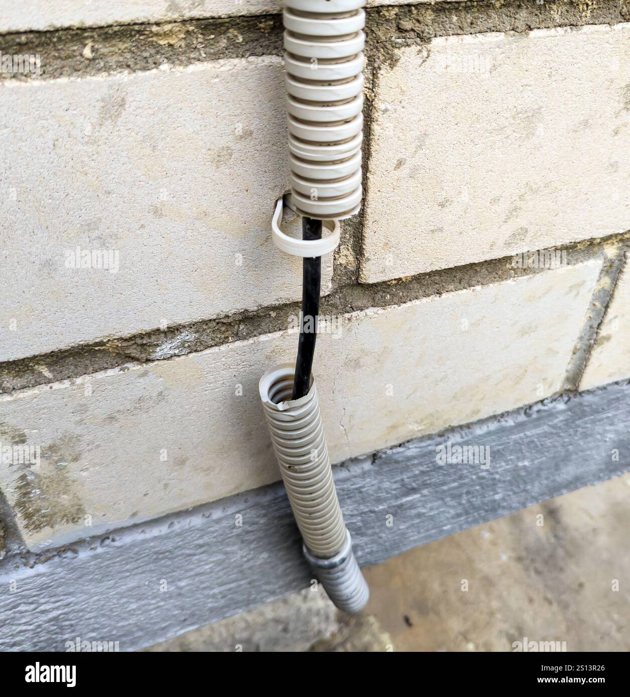 Kabel in einem abgerissenen Wellrohr an der Wand eines Gebäudes Stockfoto