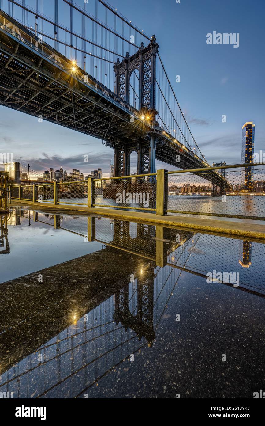 Die Manhattan Bridge in New York in der Abenddämmerung spiegelt sich in einer Pfütze wider Stockfoto