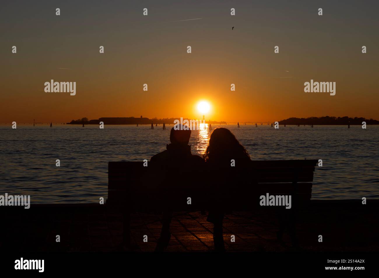 Venedig, Italien. Dezember 2024. Ein Paar (NICHT ERKENNBAR) auf einer Bank, das den Sonnenuntergang beobachtet. Stockfoto