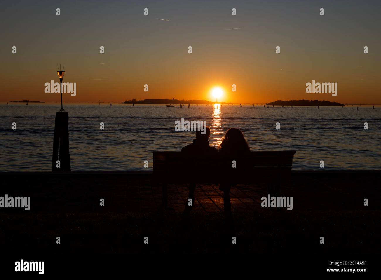 Venedig, Italien. Dezember 2024. Ein Paar (NICHT ERKENNBAR) auf einer Bank, das den Sonnenuntergang beobachtet. Stockfoto