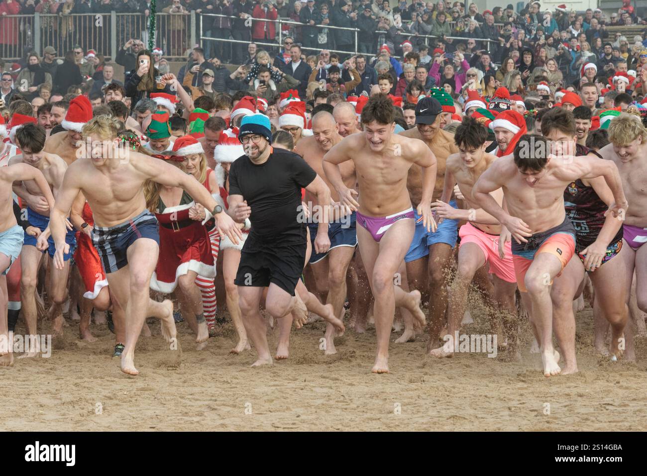 Massen von Menschen, viele in festlichen Kostümen, rasen am Exmouth Beach während des jährlichen Weihnachtstags Schwimmen in Devon, Großbritannien, 25. Dezember 2024. Stockfoto
