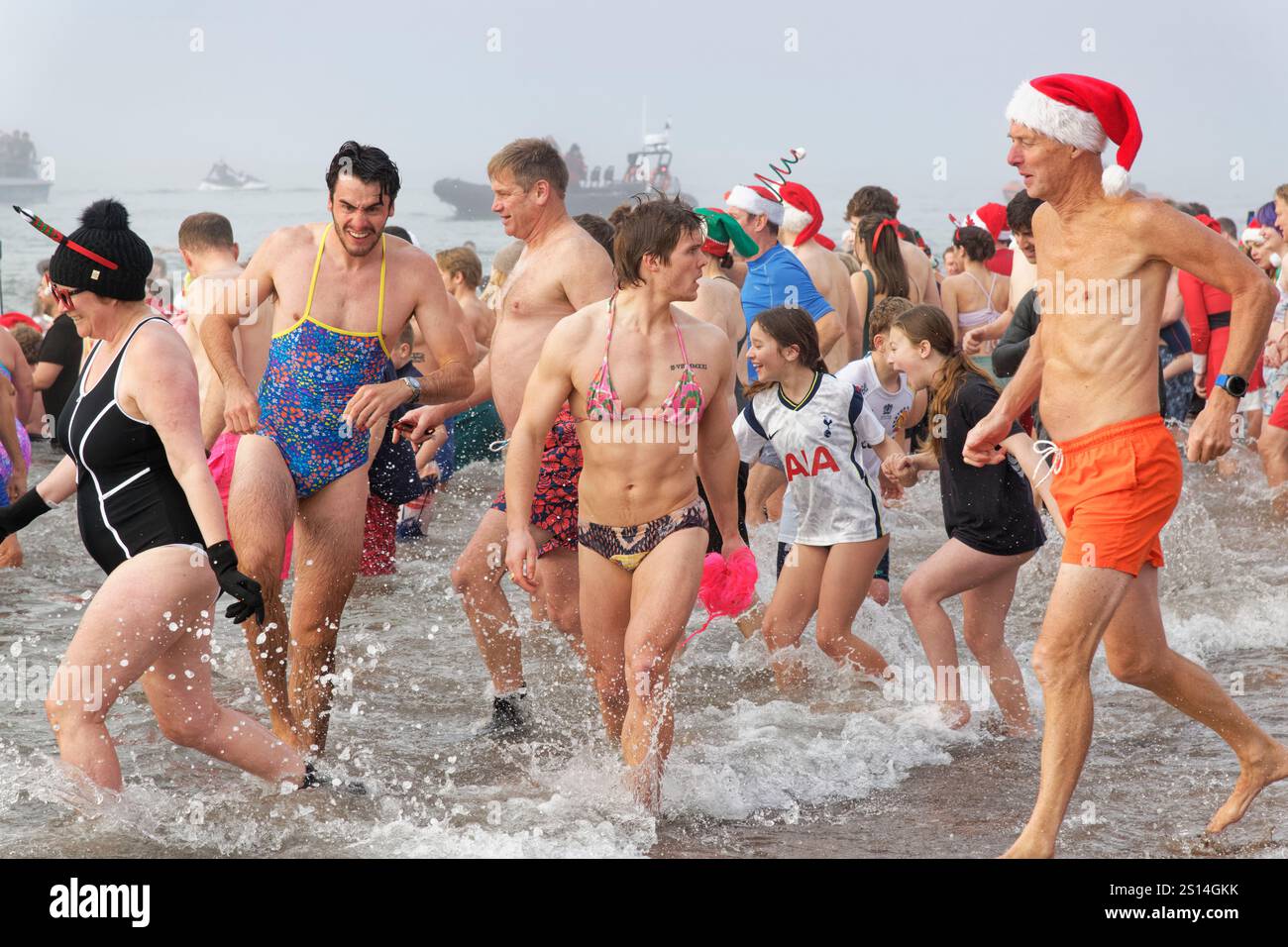 Massen von Menschen, meist in festlichen oder Comic-Kostümen, waten im Meer am Strand von Exmouth während des jährlichen Weihnachtstages Schwimmen, Devon, Großbritannien, 25. Dezember 2024. Stockfoto