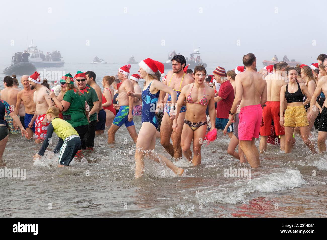 Massen von Menschen, meist in festlichen Kostümen, waten im Meer am Exmouth Beach während des jährlichen Weihnachtstages Schwimmen, Devon, Großbritannien, 25. Dezember 2024. Stockfoto
