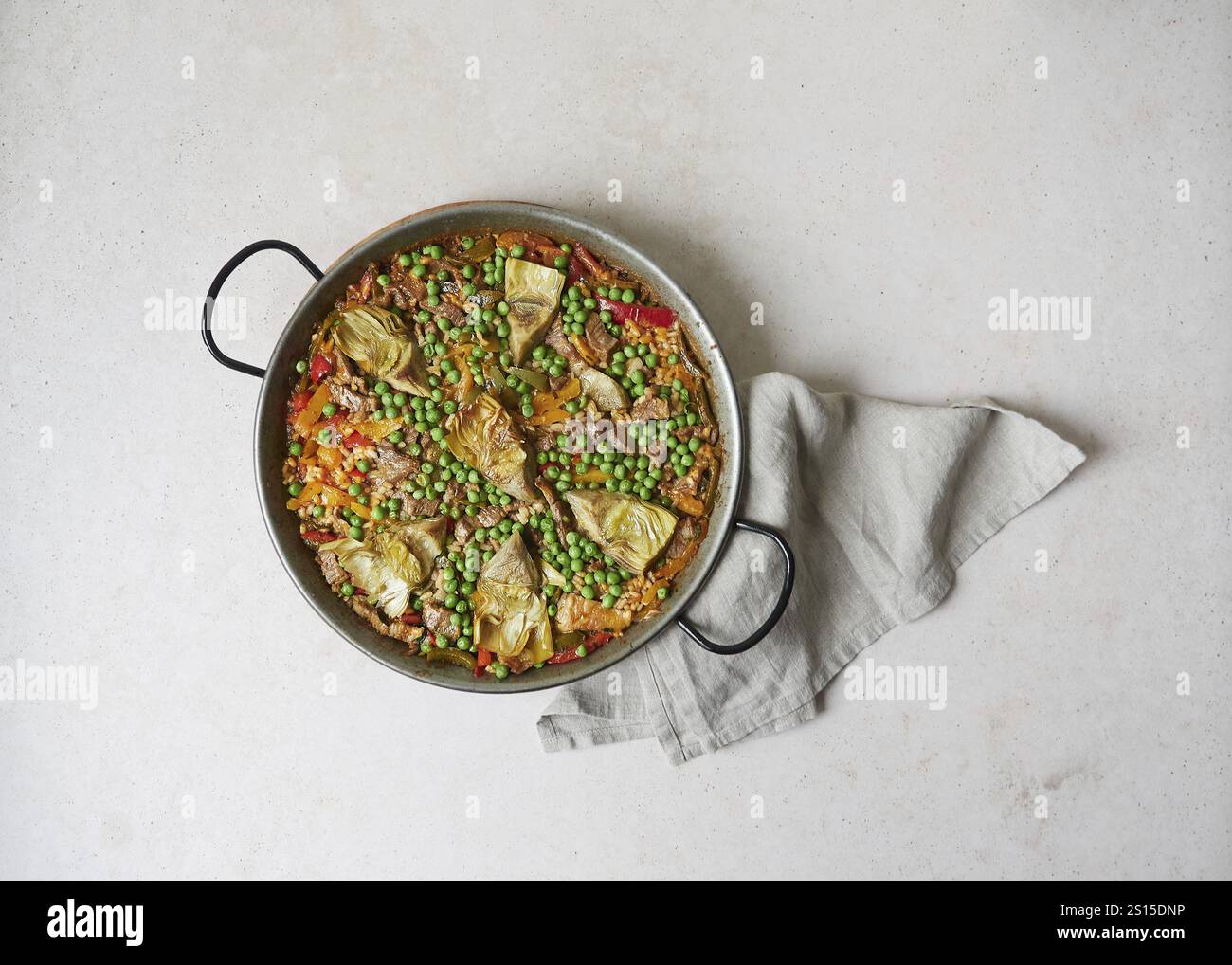 Blick von oben auf Paella in Paella Pfanne (traditionelles spanisches Utensil). Auf grauer Oberfläche mit Küchentuch unter dem Griff. Pflanzliche Zutaten, pe Stockfoto