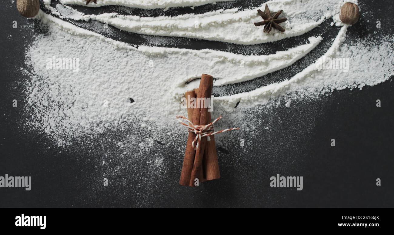 Zimtstangen, die mit Schnur gebunden sind, liegen zwischen Mehl auf einer dunklen Oberfläche Stockfoto