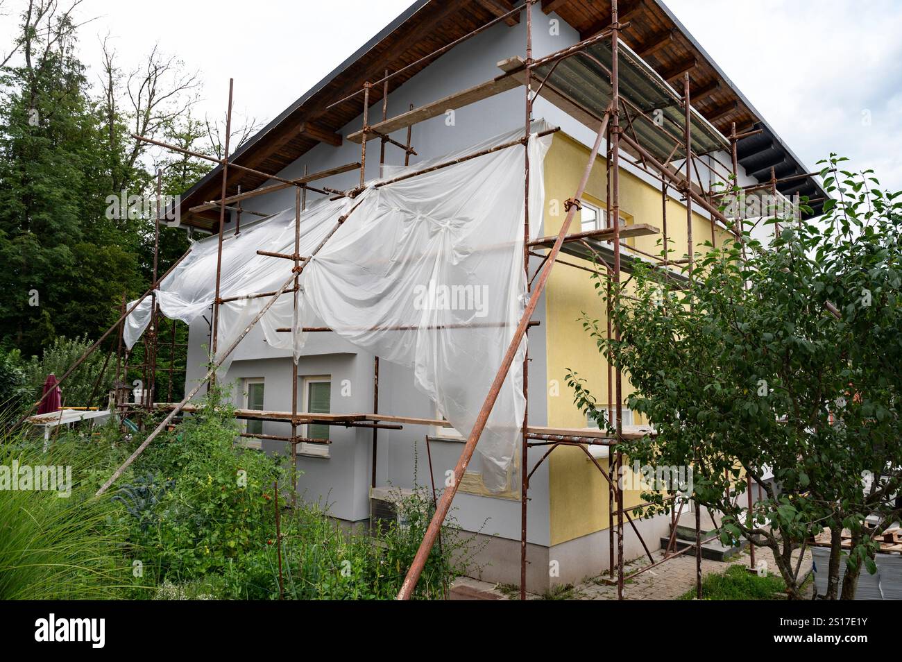 Ein Haus, das von Gerüsten und Kunststoffplatten umgeben ist, was auf die laufenden Renovierungsarbeiten im Außenbereich in einer üppigen Gartenanlage hinweist. Stockfoto