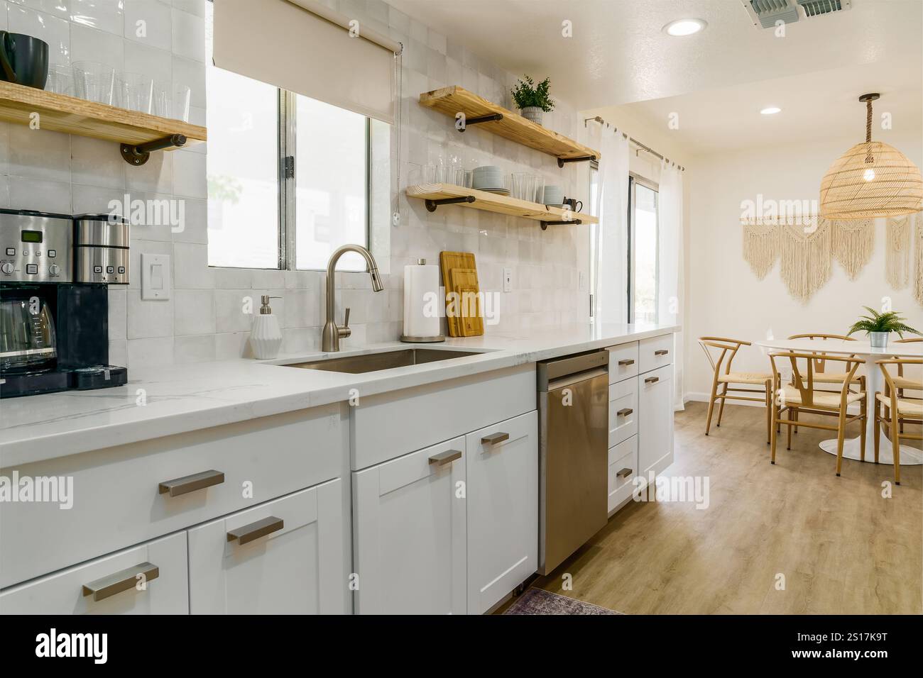 Moderne Küche mit weißen Schränken, Geräten aus Edelstahl und hellem Holzfußboden. Stockfoto