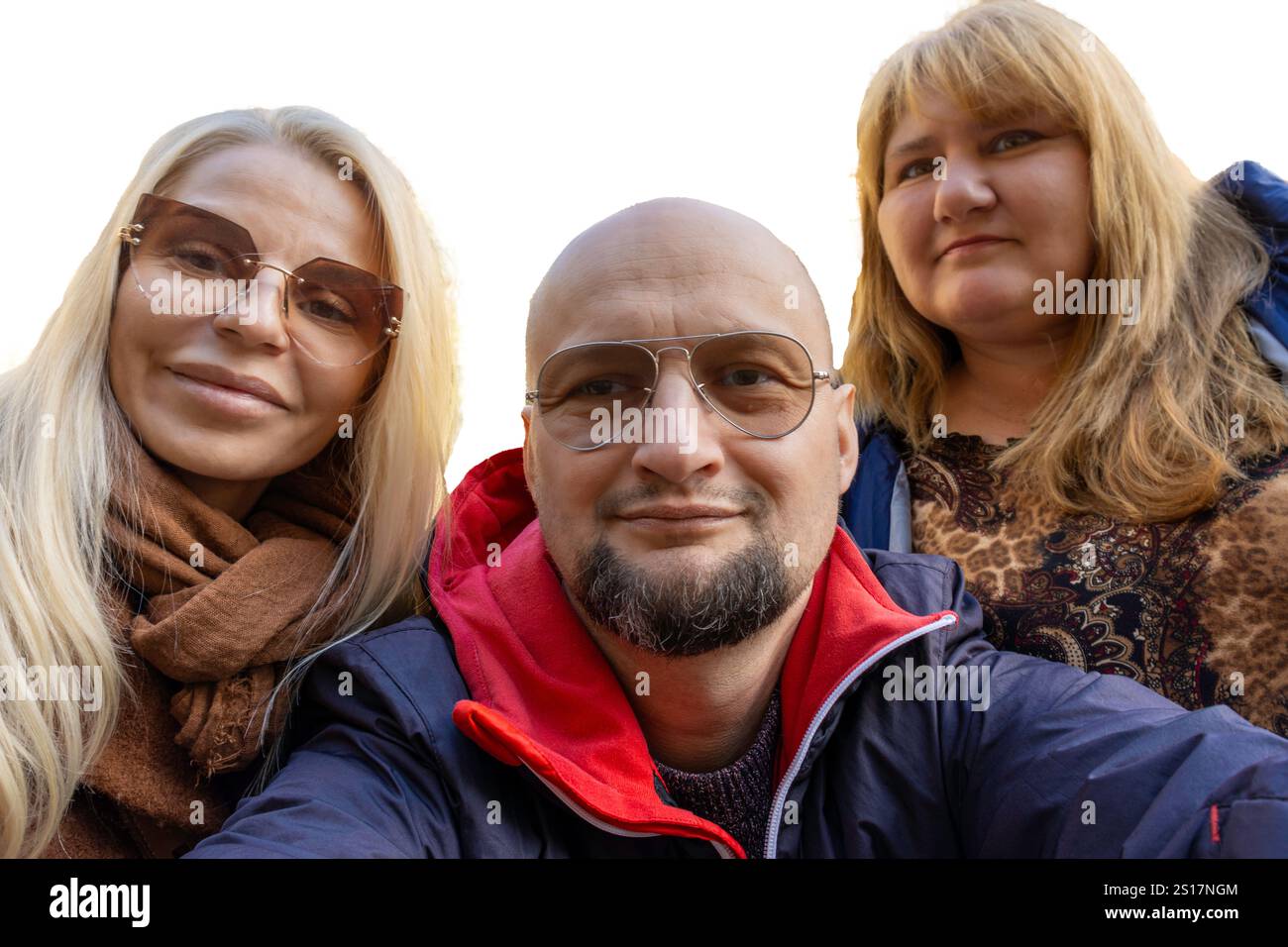 Ein fröhlicher Mann und zwei Frauen machen zusammen ein Selfie vor weißem Hintergrund, um einen fröhlichen Moment der Freundschaft und des Spaßes festzuhalten. Stockfoto