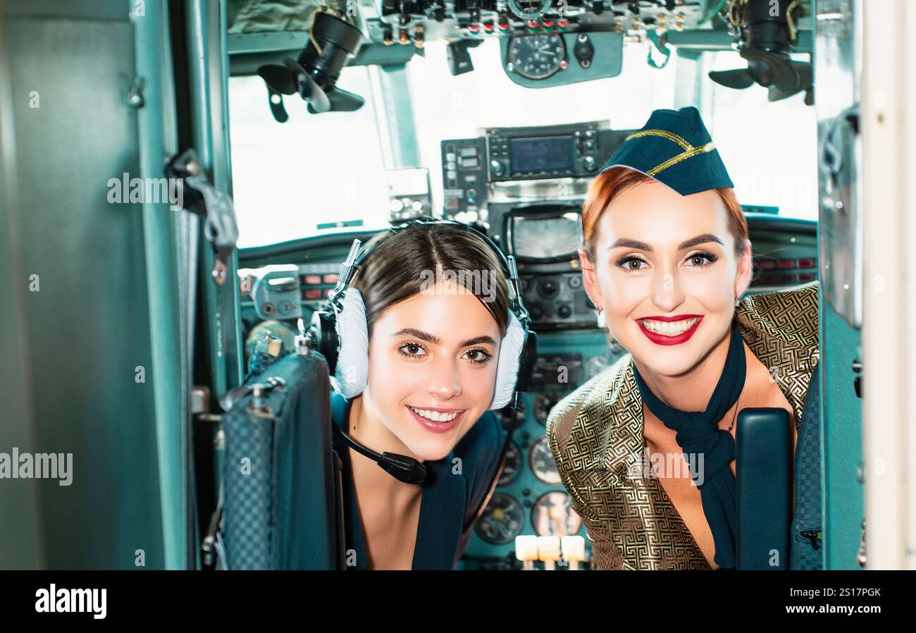 Mädchen, die die Kamera betrachten. Glücklicher und erfolgreicher Flug. Rückansicht von der Innenseite des Flugzeugs. Piloten lächeln und wünschen einen erfolgreichen Flug. Suchen Stockfoto