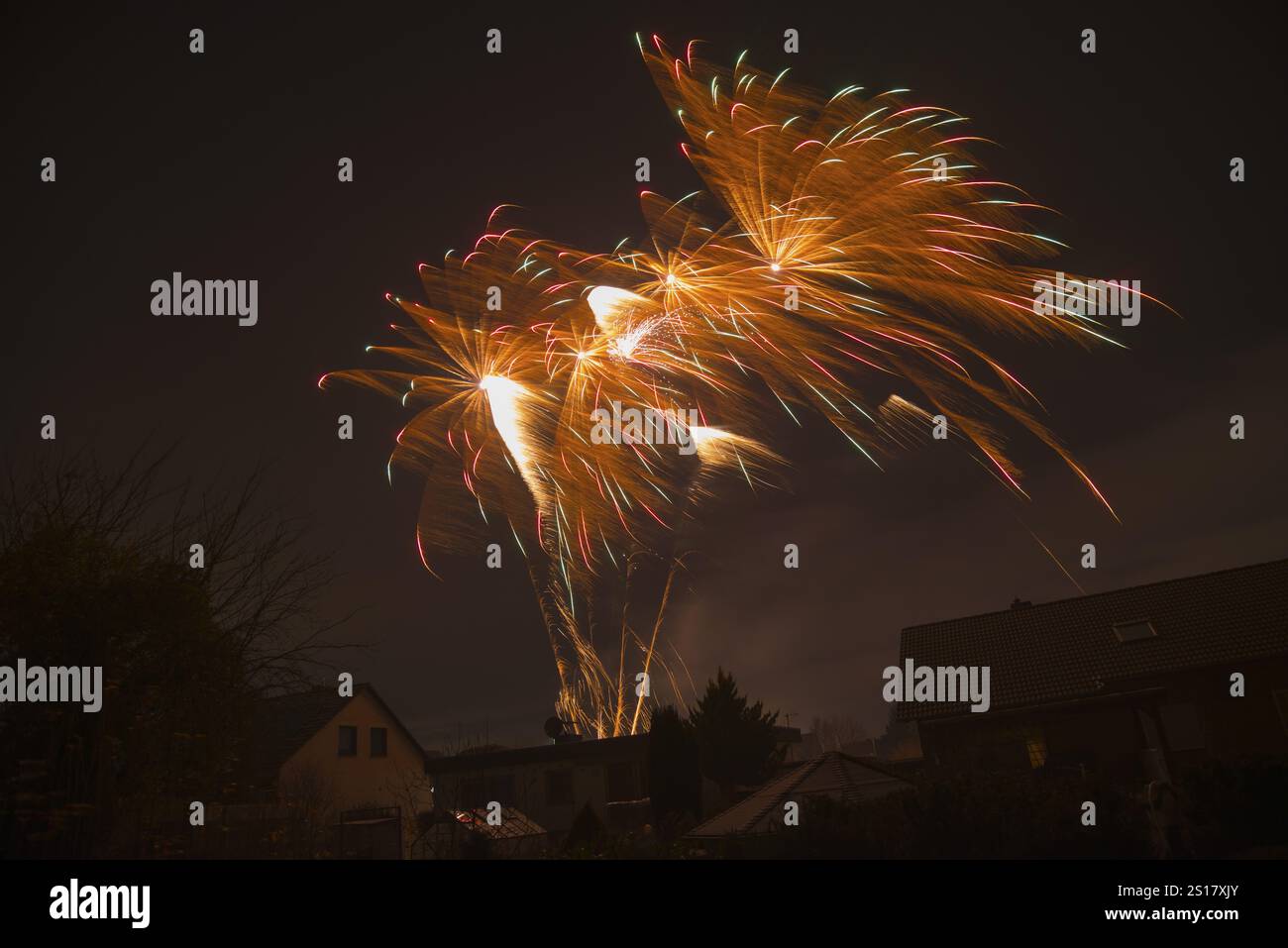 Bunte Feuerwerke über Häusern erleuchten den dunklen Nachthimmel in Ilsede, Niedersachsen, Deutschland, Europa Stockfoto