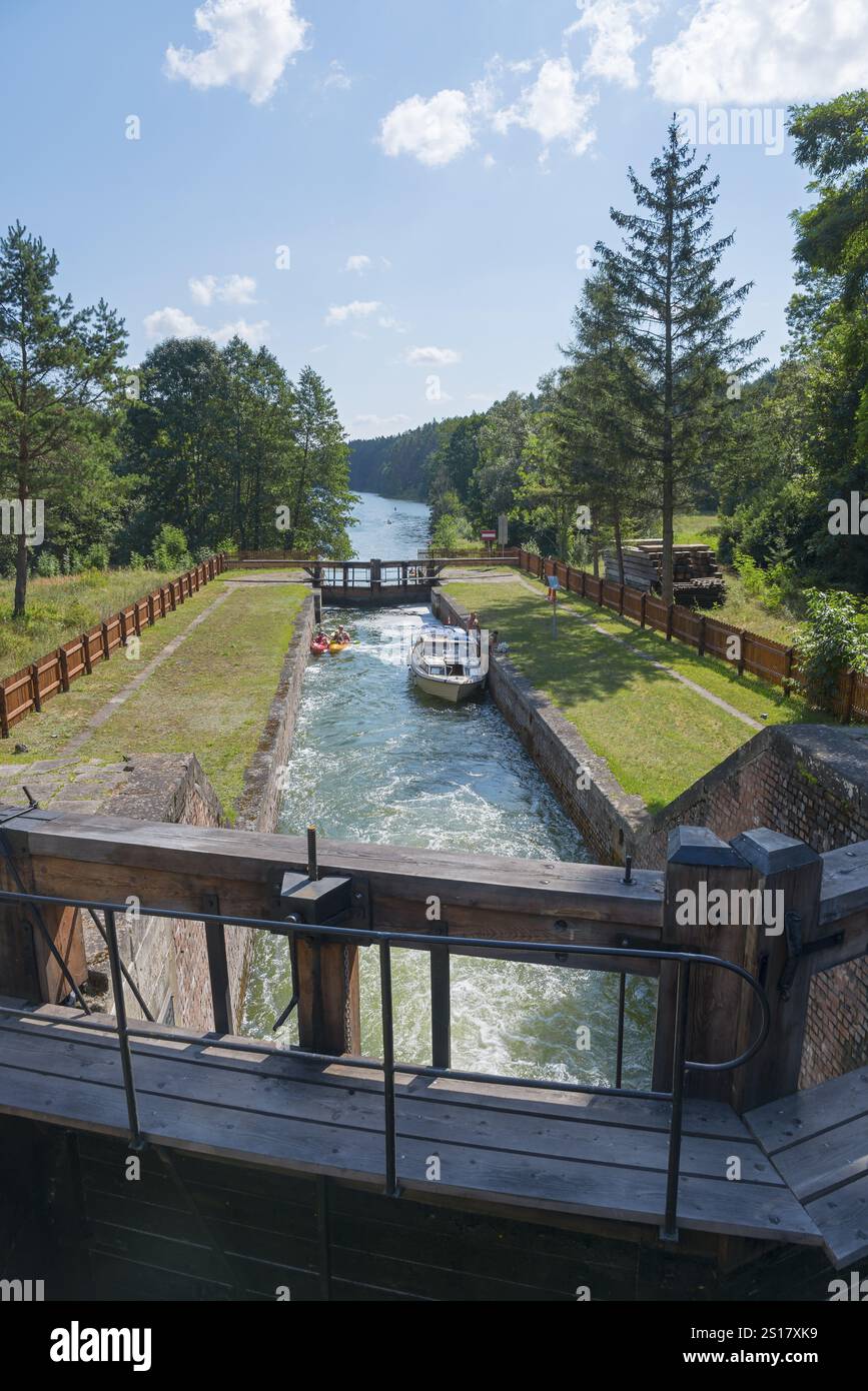 Ein Boot fährt durch die Schleuse in einer grünen, bewaldeten Landschaft unter blauem Himmel, Sluza Paniewo, Schleuse zwischen den Seen Paniewo und Krzywe, PNaska, Powiat Stockfoto